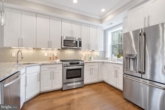 kitchen featuring appliances with stainless steel finishes, tasteful backsplash, white cabinets, sink, and light hardwood / wood-style flooring