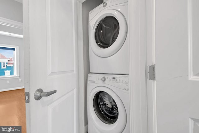 clothes washing area with hardwood / wood-style floors and stacked washer / dryer