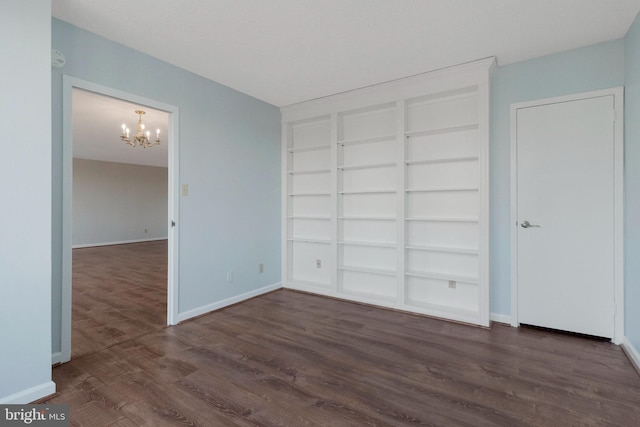 unfurnished room with built in shelves, dark hardwood / wood-style flooring, and an inviting chandelier