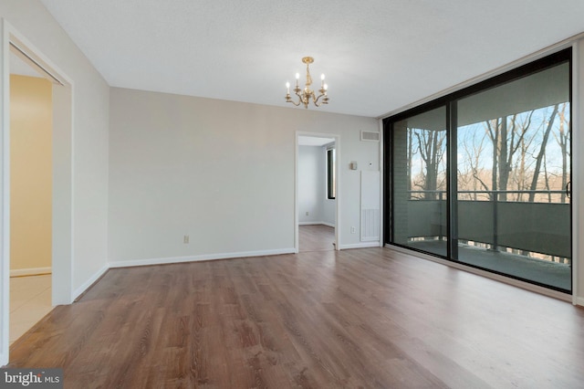 spare room featuring hardwood / wood-style flooring, a wall of windows, and an inviting chandelier