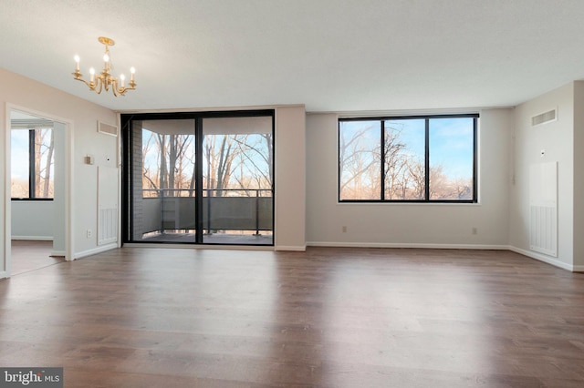 empty room with plenty of natural light, dark hardwood / wood-style floors, and a chandelier