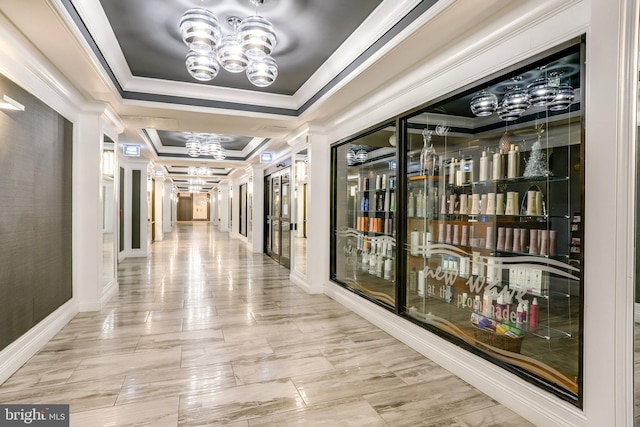 hall with a raised ceiling, ornamental molding, and an inviting chandelier