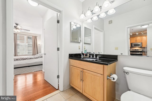 bathroom with rail lighting, ceiling fan, vanity, wood-type flooring, and toilet