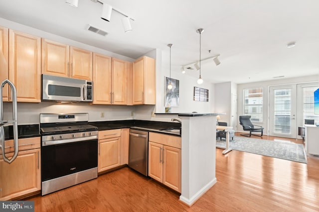 kitchen with sink, appliances with stainless steel finishes, decorative light fixtures, kitchen peninsula, and light wood-type flooring