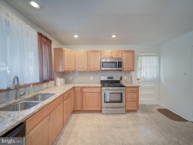 kitchen featuring sink, backsplash, light stone countertops, and appliances with stainless steel finishes