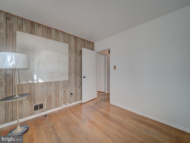 unfurnished room featuring wooden walls and light hardwood / wood-style flooring