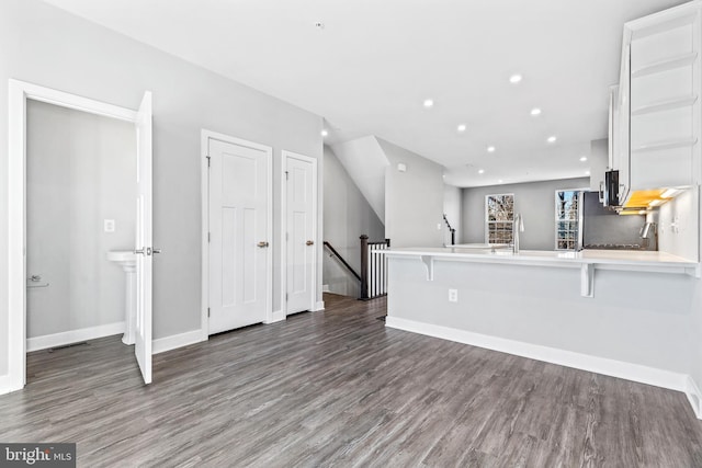 kitchen featuring a breakfast bar, appliances with stainless steel finishes, white cabinets, dark hardwood / wood-style flooring, and kitchen peninsula