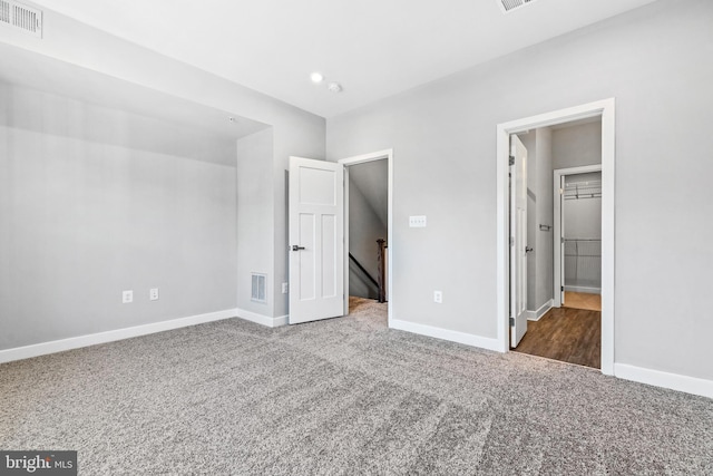 unfurnished bedroom with dark colored carpet, a walk in closet, and a closet