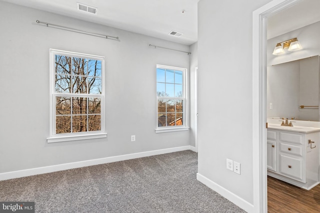 unfurnished bedroom with connected bathroom, sink, and dark colored carpet