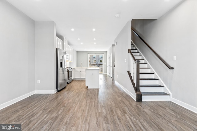 kitchen with sink, appliances with stainless steel finishes, white cabinetry, hardwood / wood-style floors, and a center island