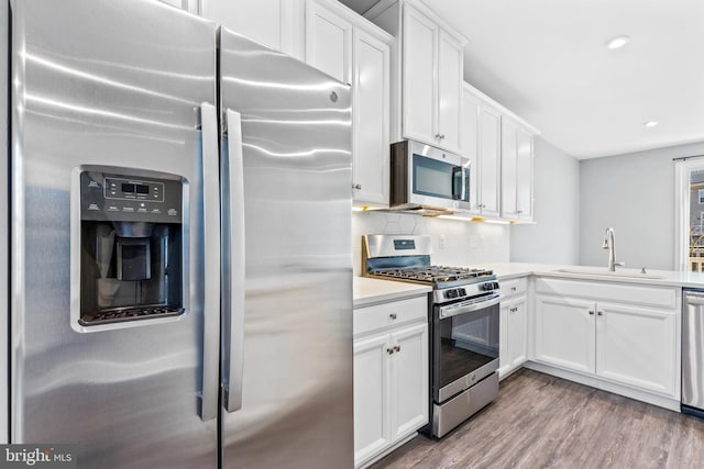 kitchen with sink, light hardwood / wood-style flooring, white cabinets, stainless steel appliances, and backsplash