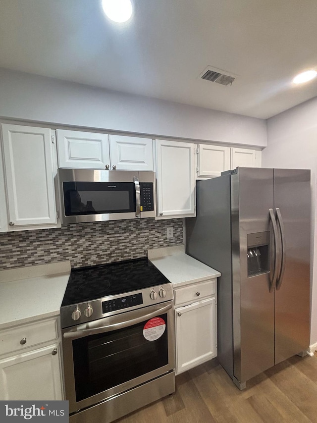 kitchen with stainless steel appliances, white cabinetry, tasteful backsplash, and wood-type flooring