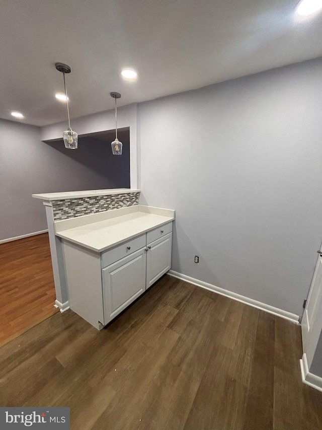 kitchen featuring kitchen peninsula, pendant lighting, backsplash, white cabinetry, and dark hardwood / wood-style floors