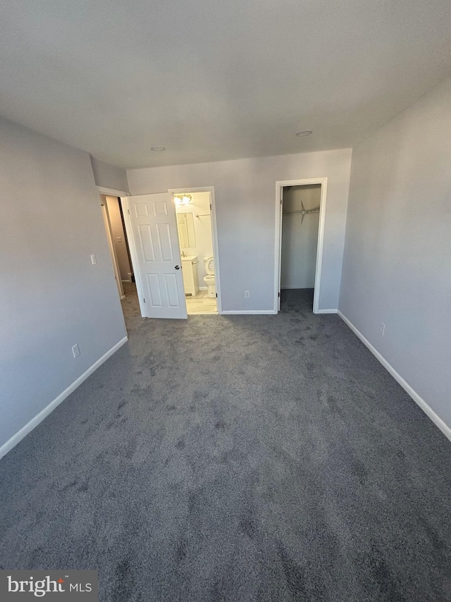 unfurnished bedroom featuring a closet, carpet flooring, a walk in closet, and ensuite bath