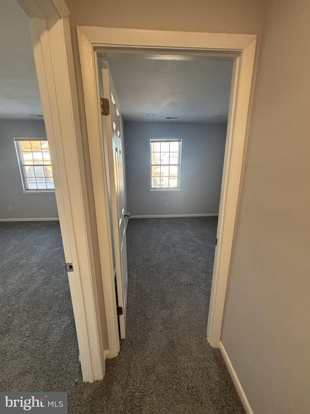 hallway featuring dark colored carpet and plenty of natural light