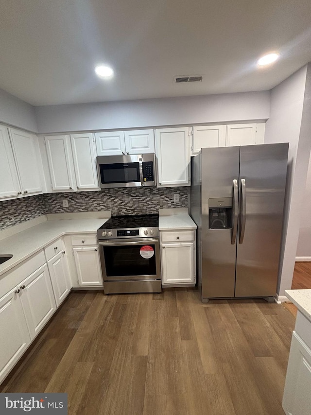 kitchen with white cabinets, dark hardwood / wood-style flooring, appliances with stainless steel finishes, and decorative backsplash