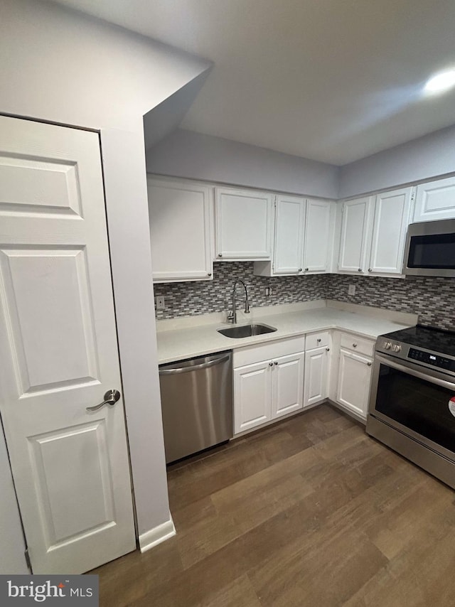 kitchen with appliances with stainless steel finishes, sink, white cabinets, tasteful backsplash, and dark wood-type flooring