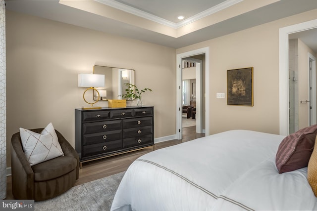 bedroom featuring a raised ceiling, ornamental molding, dark wood-type flooring, and ensuite bath