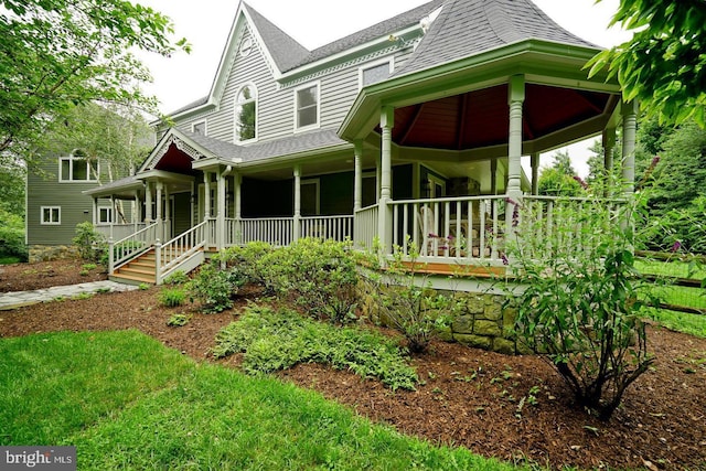 victorian home featuring covered porch and roof with shingles