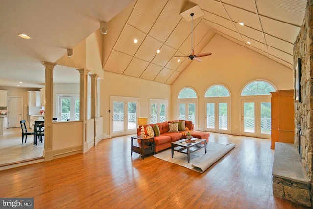 living room featuring high vaulted ceiling, decorative columns, light wood-style flooring, and a ceiling fan