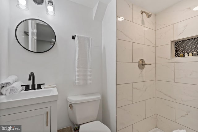 bathroom featuring vanity, a tile shower, and toilet