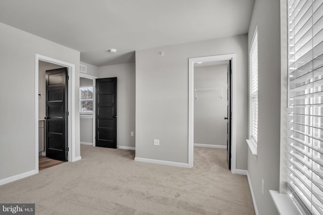 unfurnished bedroom with multiple windows, a closet, a spacious closet, and light carpet