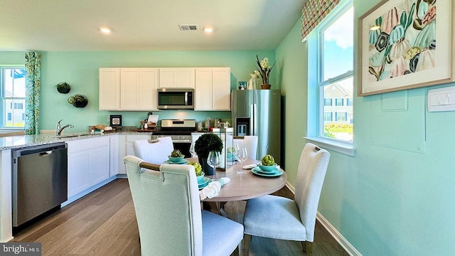 kitchen with hardwood / wood-style floors, white cabinets, stainless steel appliances, light stone counters, and plenty of natural light