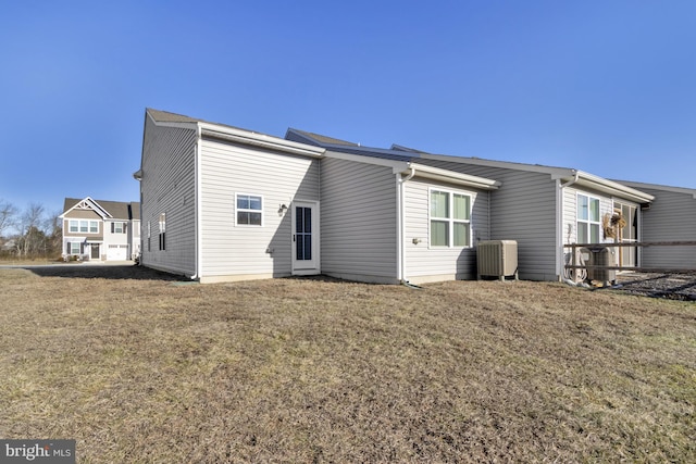 rear view of house with central AC unit and a lawn