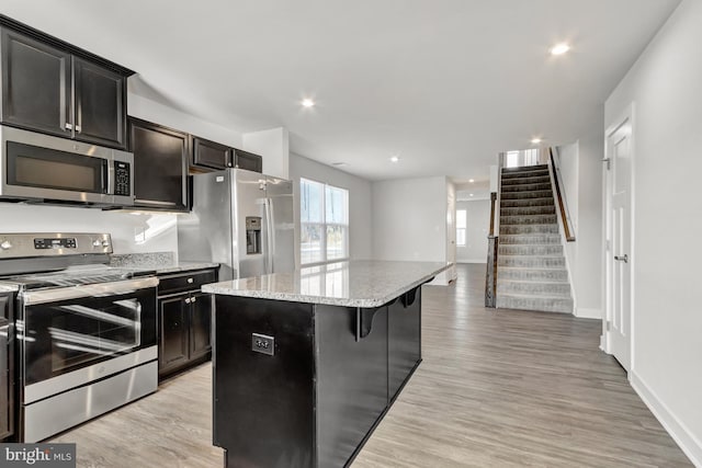 kitchen with a kitchen island, a kitchen bar, light stone counters, light hardwood / wood-style floors, and stainless steel appliances