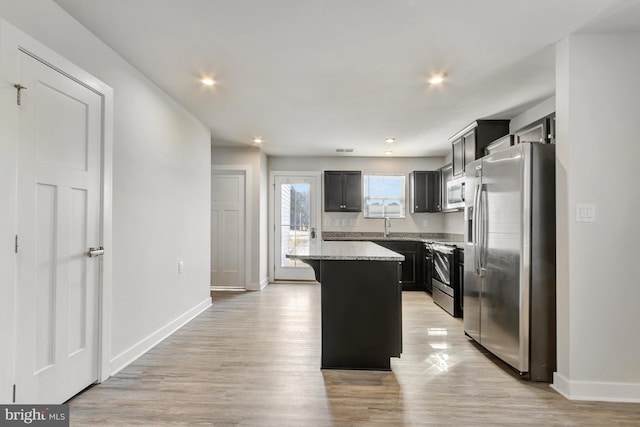 kitchen with light stone counters, light hardwood / wood-style flooring, a kitchen breakfast bar, a kitchen island, and stainless steel appliances