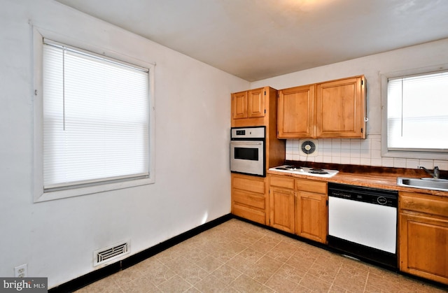 kitchen featuring white stovetop, sink, tasteful backsplash, dishwashing machine, and oven