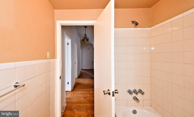 bathroom featuring hardwood / wood-style flooring, tiled shower / bath combo, and tile walls