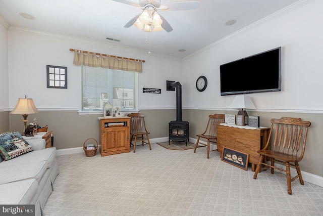 living room featuring light carpet, ornamental molding, ceiling fan, and a wood stove