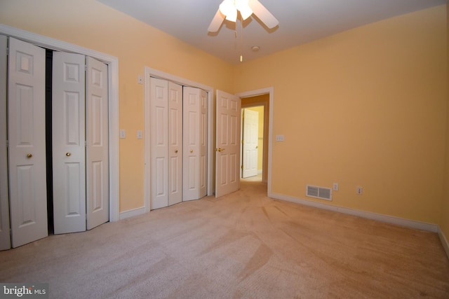 unfurnished bedroom with two closets, light colored carpet, and ceiling fan