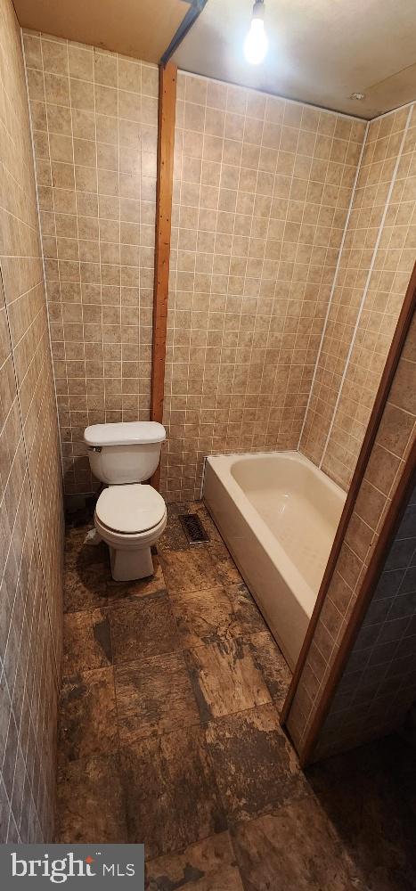 bathroom with a tub to relax in, toilet, and tile walls