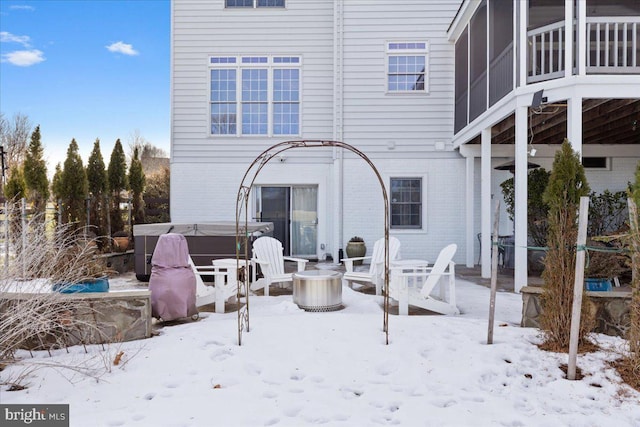 snow covered back of property with a fire pit and a hot tub