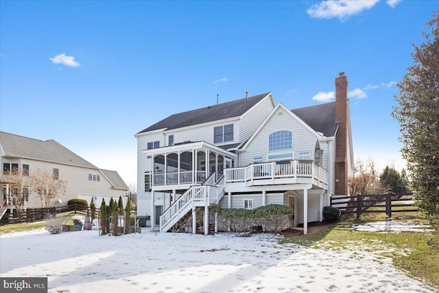 snow covered back of property with a sunroom and a deck