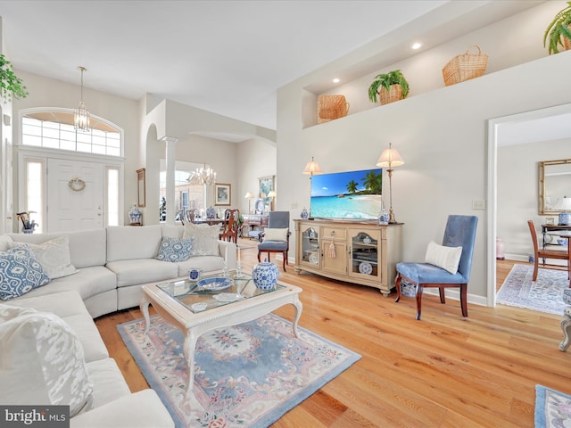 living room featuring decorative columns, wood-type flooring, a towering ceiling, and a chandelier