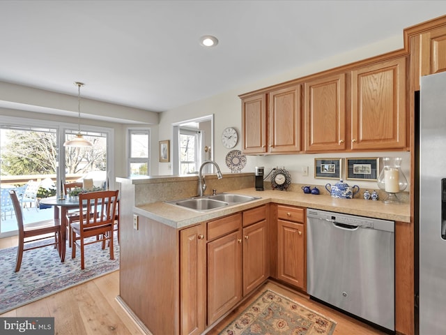 kitchen featuring sink, hanging light fixtures, appliances with stainless steel finishes, kitchen peninsula, and light hardwood / wood-style floors