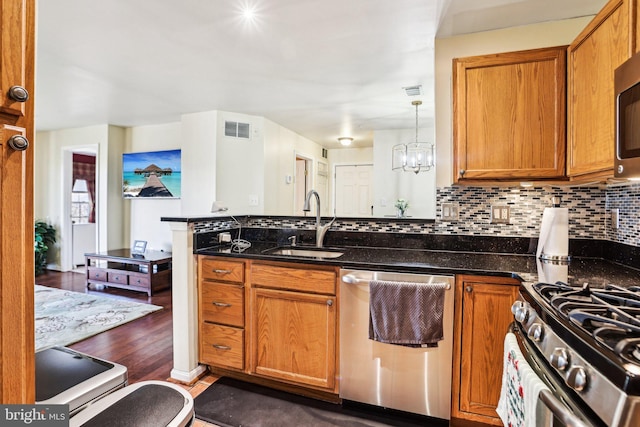 kitchen with appliances with stainless steel finishes, decorative light fixtures, sink, and dark stone countertops