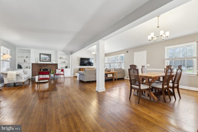 dining area featuring baseboards, built in features, a chandelier, a fireplace, and wood-type flooring