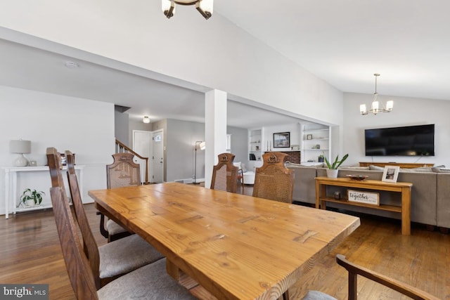 dining space featuring a chandelier, lofted ceiling, built in shelves, and wood finished floors
