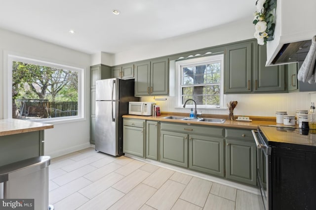 kitchen featuring stainless steel appliances, light countertops, premium range hood, and a sink