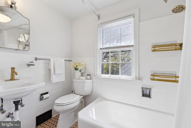 bathroom with toilet, a washtub, wainscoting, visible vents, and tile walls