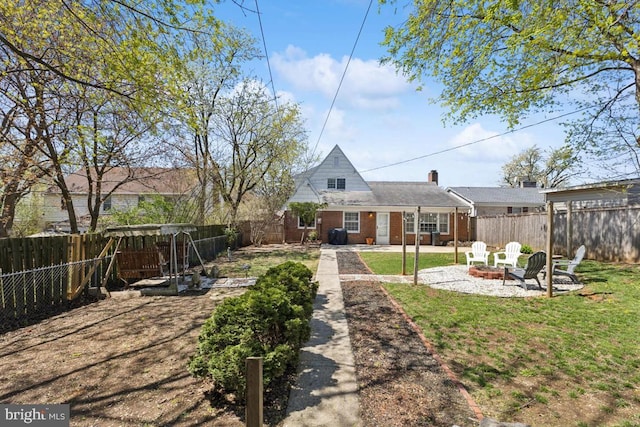 back of house featuring a patio area, an outdoor fire pit, a yard, a fenced backyard, and brick siding