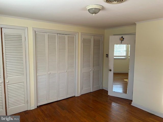 unfurnished bedroom with crown molding, dark wood-type flooring, and two closets