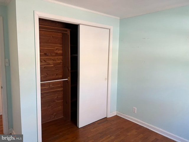 unfurnished bedroom with dark hardwood / wood-style flooring, crown molding, and a closet