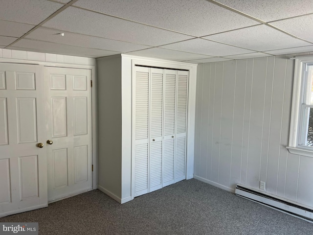 unfurnished bedroom with a paneled ceiling, dark colored carpet, a closet, and baseboard heating