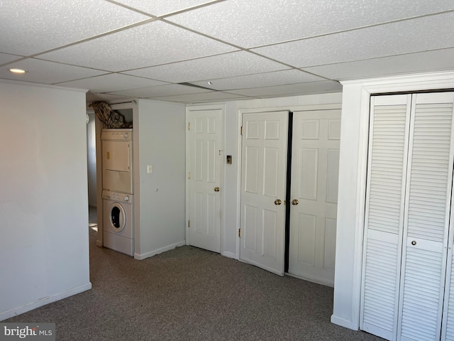 basement featuring a drop ceiling, carpet floors, and stacked washer and clothes dryer