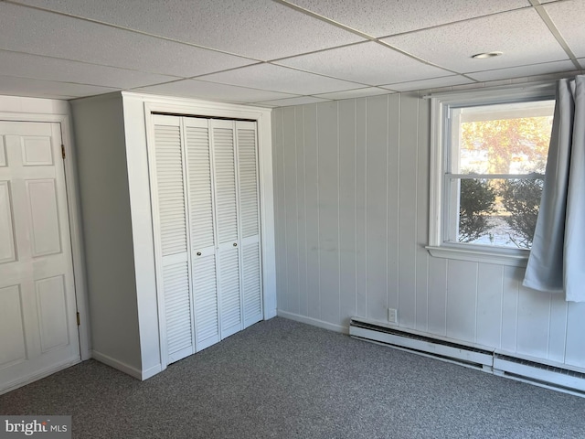 unfurnished bedroom with a baseboard radiator, carpet, a closet, and a drop ceiling